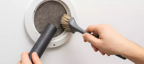 "Person rengör filter i frånluftsventilation med borste och dammsugare – regelbundet underhåll för bättre luftcirkulation och renare inomhusluft"